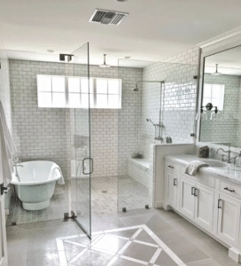 A spacious, light-filled bathroom features geometric floor tiles, white subway tile walls, a freestanding tub, and a large seamless glass shower