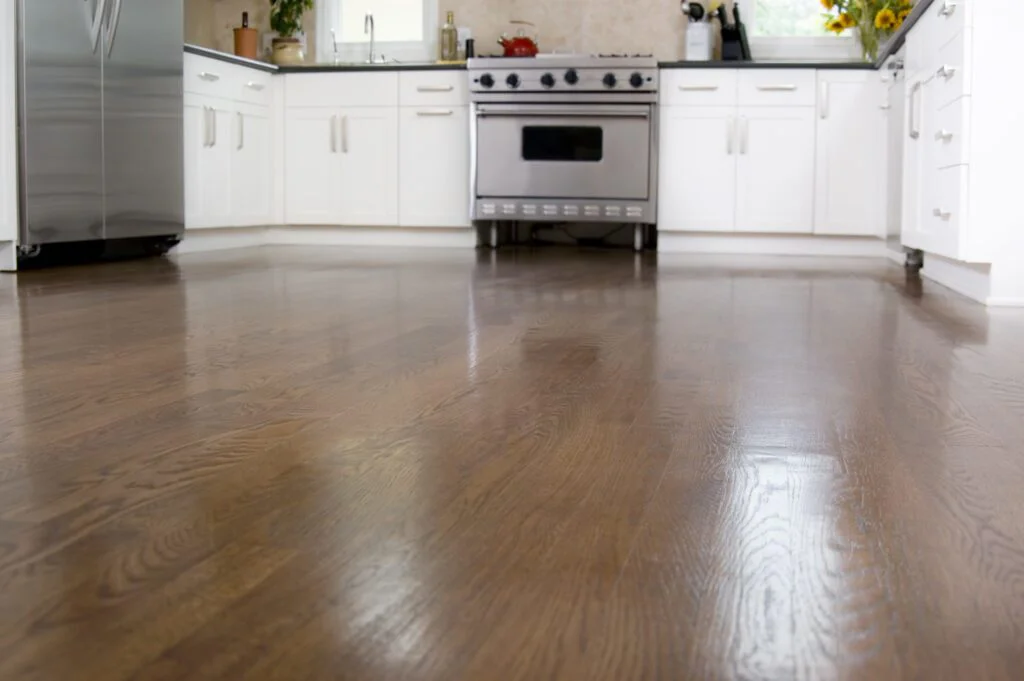 A modern kitchen features gleaming dark wood floors, white cabinets, and stainless steel appliances