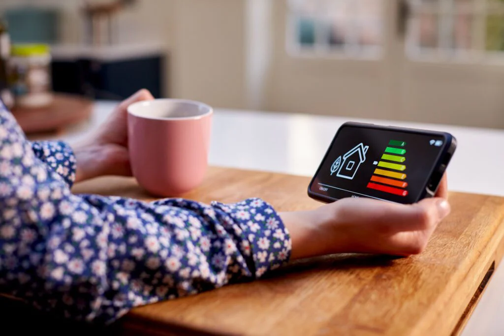 A person holds a phone displaying a home's energy efficiency rating and a pink mug