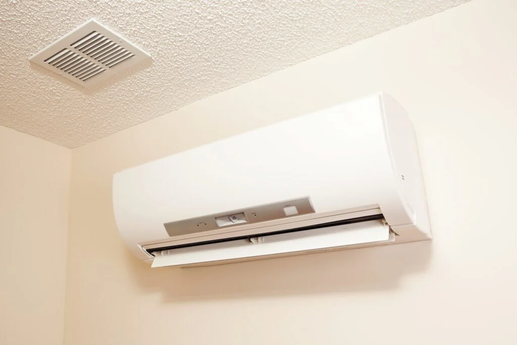 A white mini-split air conditioner unit is mounted on a light wall, with a ceiling vent above