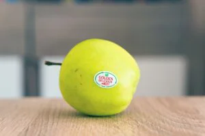A vibrant green Golden Delicious apple with brand sticker on a table